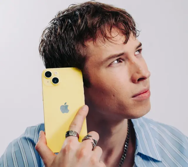 Ung man med gul iPhone mot örat, ser fundersam ut. Kanske är det dåligt ljud i iPhonen som gör honom bekymrad.