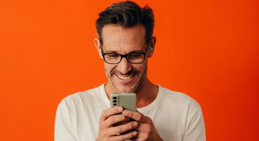 Man med glasögon och hörlurar ler när han tittar på sin iPhone.