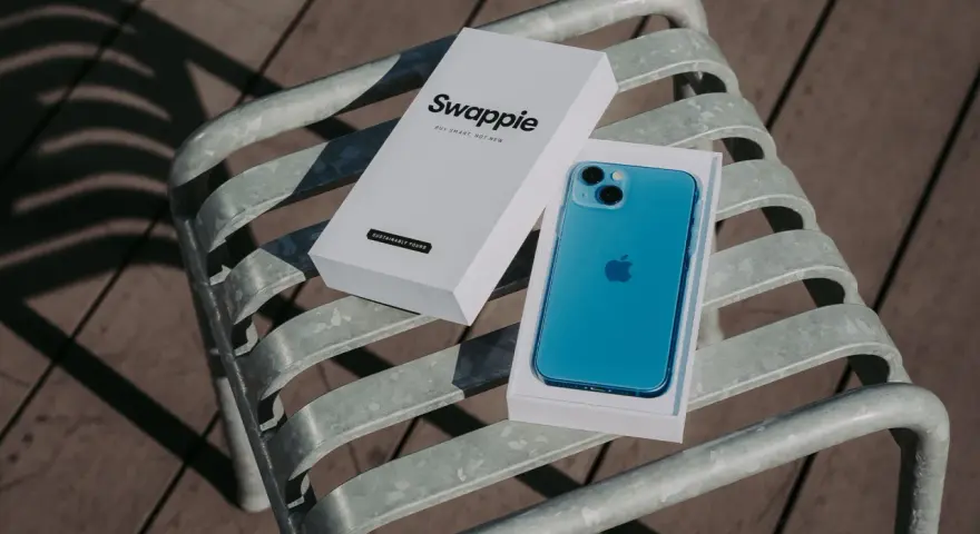 En blå iPhone 13 med Swappie-förpackning på en bänk. Denna iPhone 13 kamera är redo att fånga dina minnen.