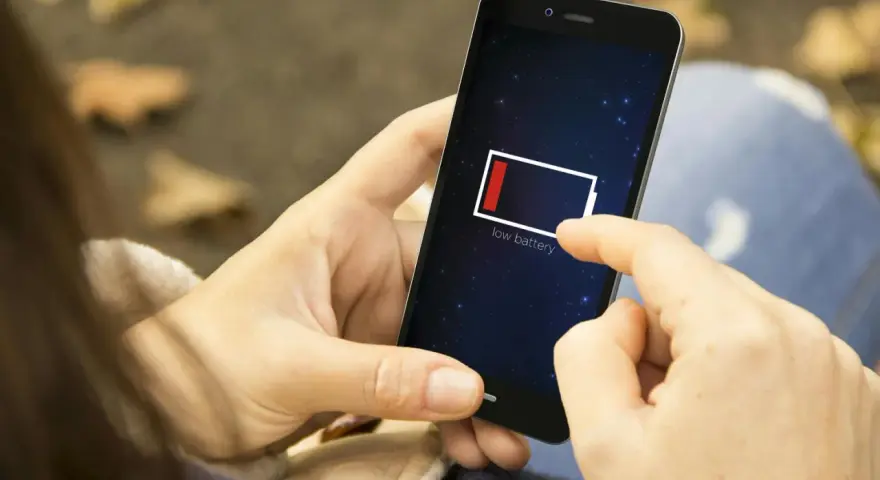 En person håller en mobil med lågt batteri. Det är mörkt ute, som om mobilen drar batteri på natten.