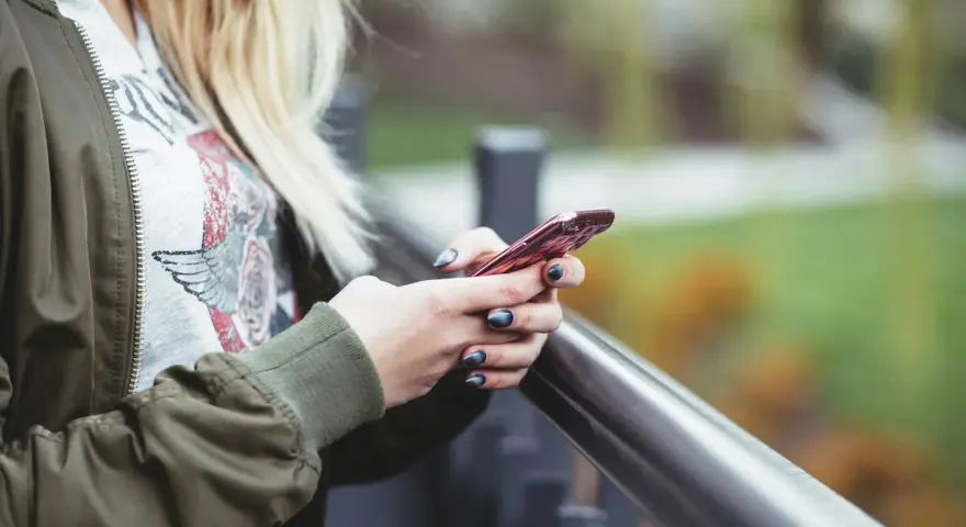 En person med blont hår håller en rosa iPhone. Snabbstart iPhone funkar inte, frustrerad över tekniken.