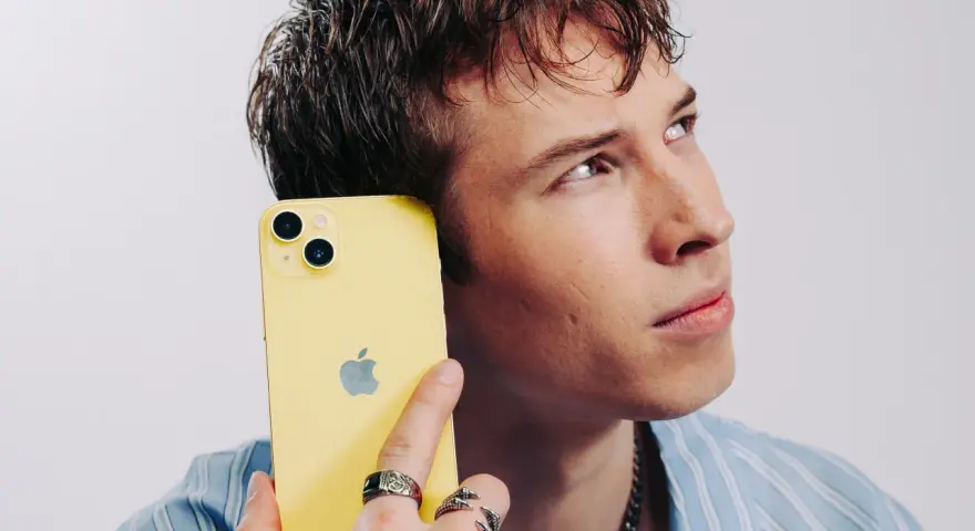Ung man med gul iPhone mot örat, ser fundersam ut. Kanske är det dåligt ljud i iPhonen som gör honom bekymrad.