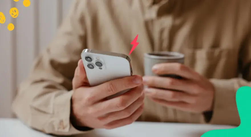 En person håller en iPhone och en mugg. En blixtsymbol indikerar att batterikapacitet iPhone är låg.