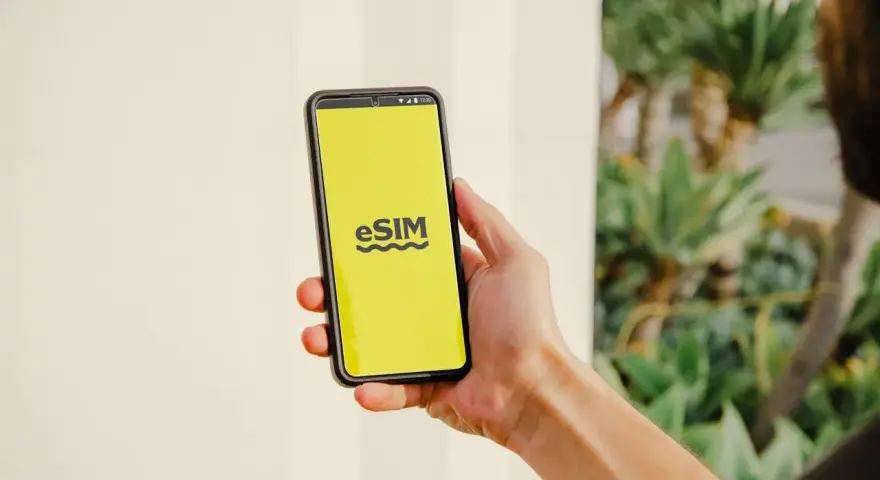 En hand håller en telefon med en gul skärm som visar "eSIM". Dags att byta SIMkort till ett eSIM för en smidigare upplevelse.