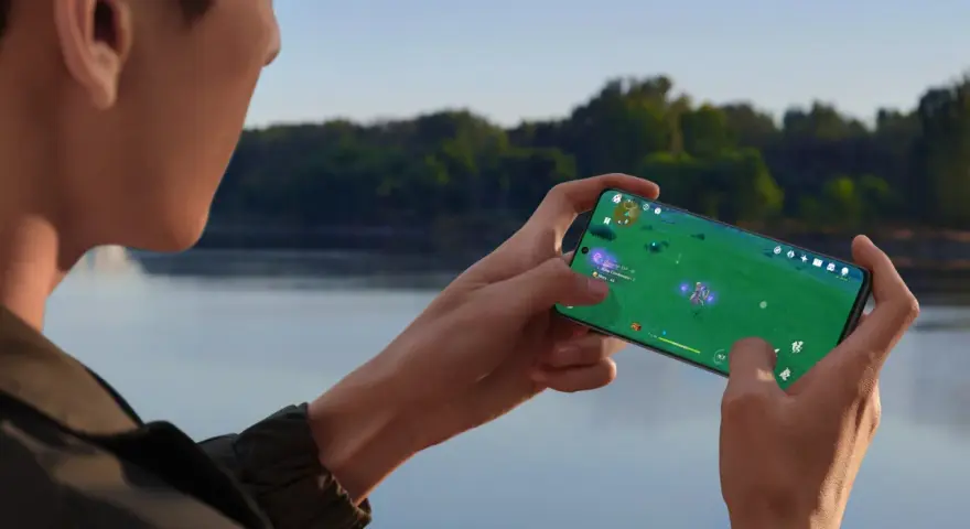 Person spelar mobilspel vid vattnet. Telefonen blir varm och drar batteri, men spelet är fängslande.