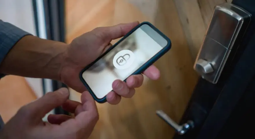 En person håller en iPhone 6 med en upplåsningsikon på skärmen, redo att låsa upp dörren.