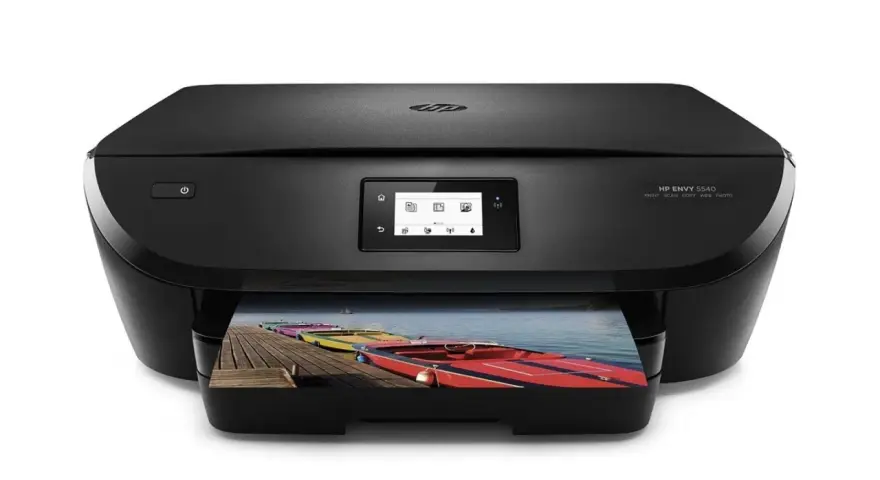 Svart HP Envy 5540-skrivare som skriver ut ett foto av färgglada båtar på en brygga. Enkel att skriva ut från iPhone.