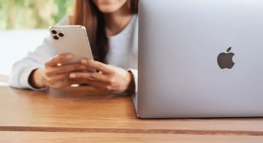 Person använder en iPhone för att skicka bilder från Samsung till iPhone. En MacBook ligger bredvid.