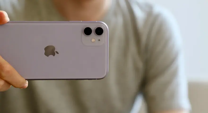 En person håller upp en lila iPhone 11. Man ser tydligt den dubbla iphone 11 kameran på baksidan.