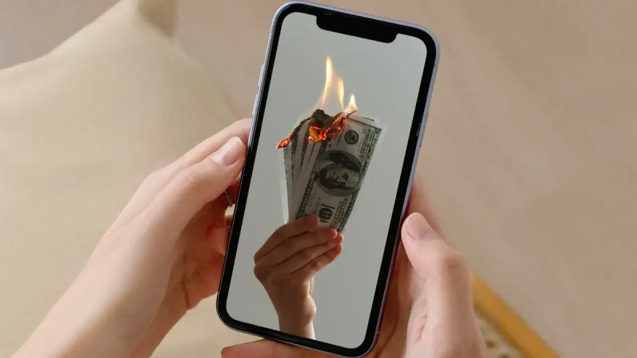 En hand håller en mobil där sedlar brinner. Kanske en bild av en misslyckad apple återbetalning.