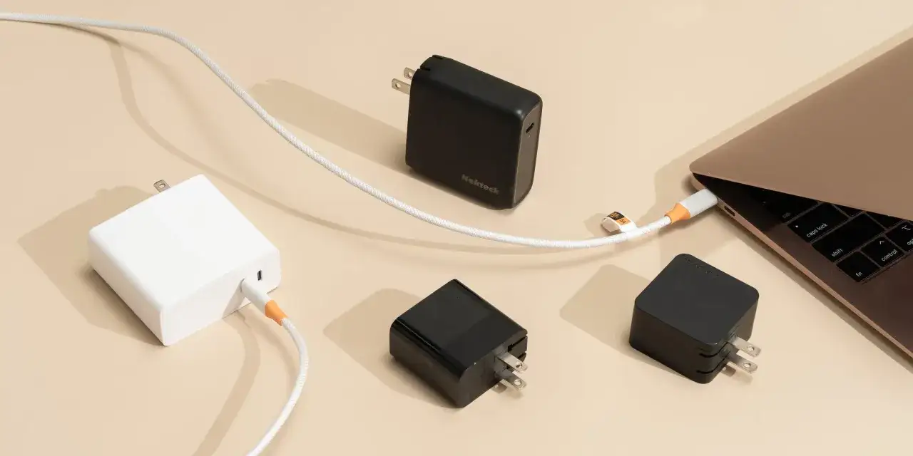 Flera laddare, en vit och tv&aring; svarta, ligger utspridda. En vit kabel &auml;r ansluten till en laptop f&ouml;r att ladda mobil med datorladdare.
