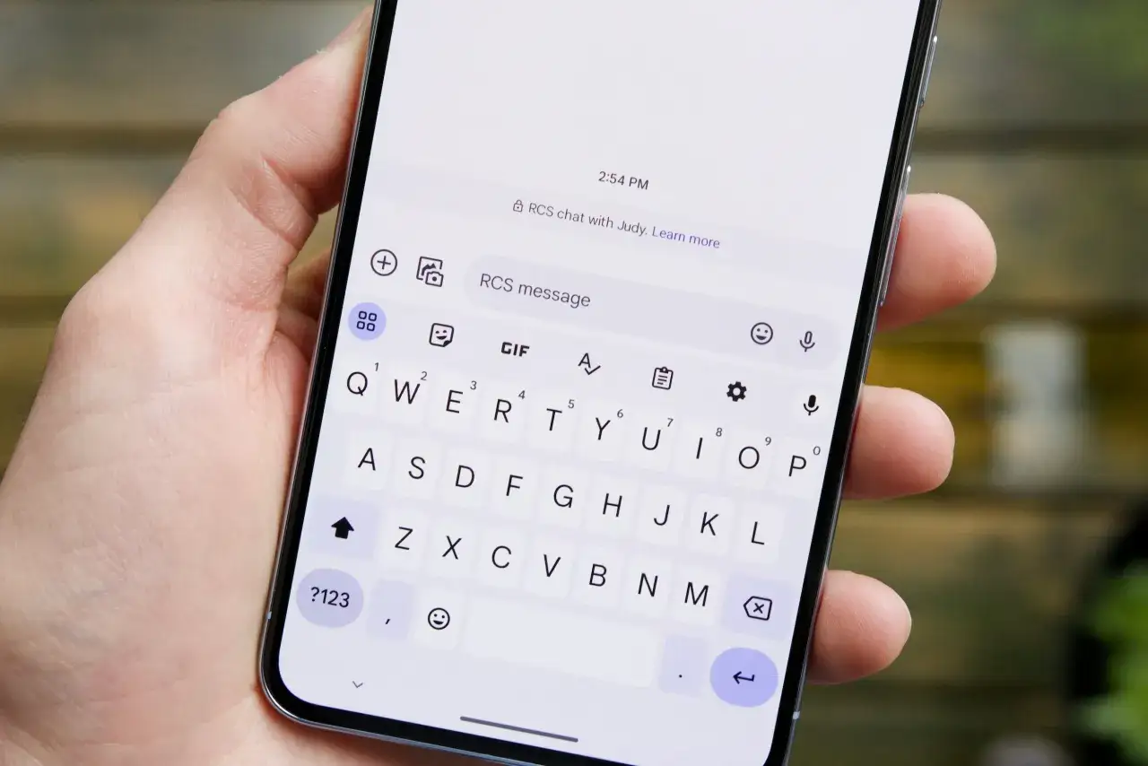 En hand håller en mobiltelefon med ett tangentbord synligt. Ett RCS-meddelande visas på skärmen, redo att skickas.