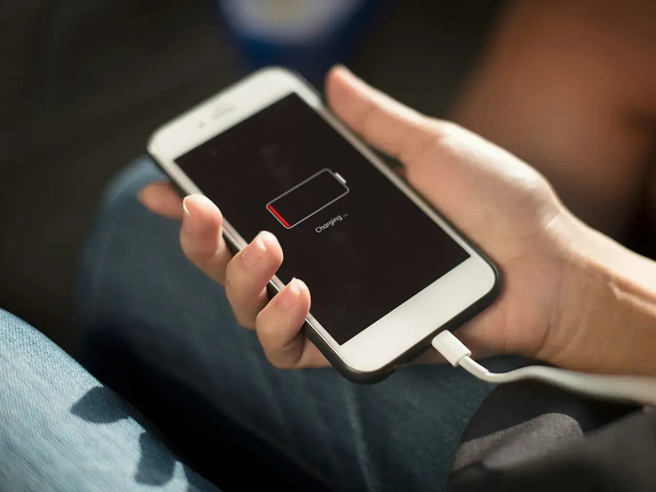 En hand håller en mobil som laddas. Batteriikonen visar att mobilen drar batteri på natten, trots laddkabeln.