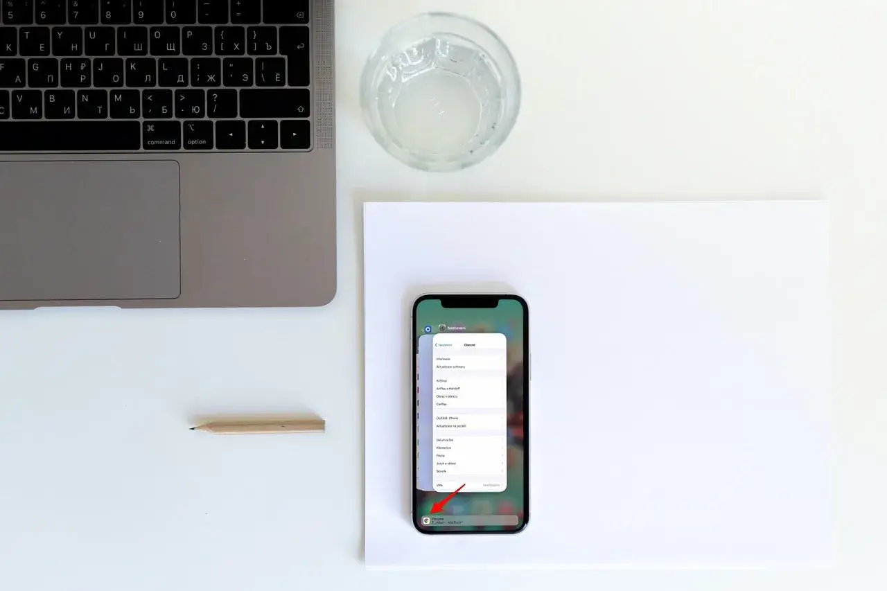 Urklipp iPhone visar inst&auml;llningar. Bredvid en laptop och ett glas vatten.