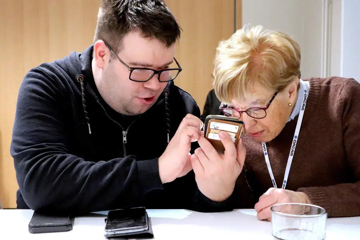 Man och kvinna tittar p&aring; en telefon. Kvinnan anv&auml;nder en f&ouml;rstoringsglasfunktion p&aring; telefonen, en hj&auml;lp f&ouml;r synskadade.