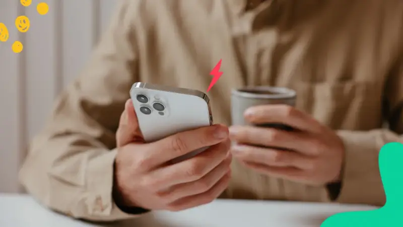 En person håller en iPhone och en mugg. En blixtsymbol indikerar att batterikapacitet iPhone är låg.
