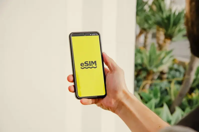 En hand håller en telefon med en gul skärm som visar "eSIM". Dags att byta SIMkort till ett eSIM för en smidigare upplevelse.